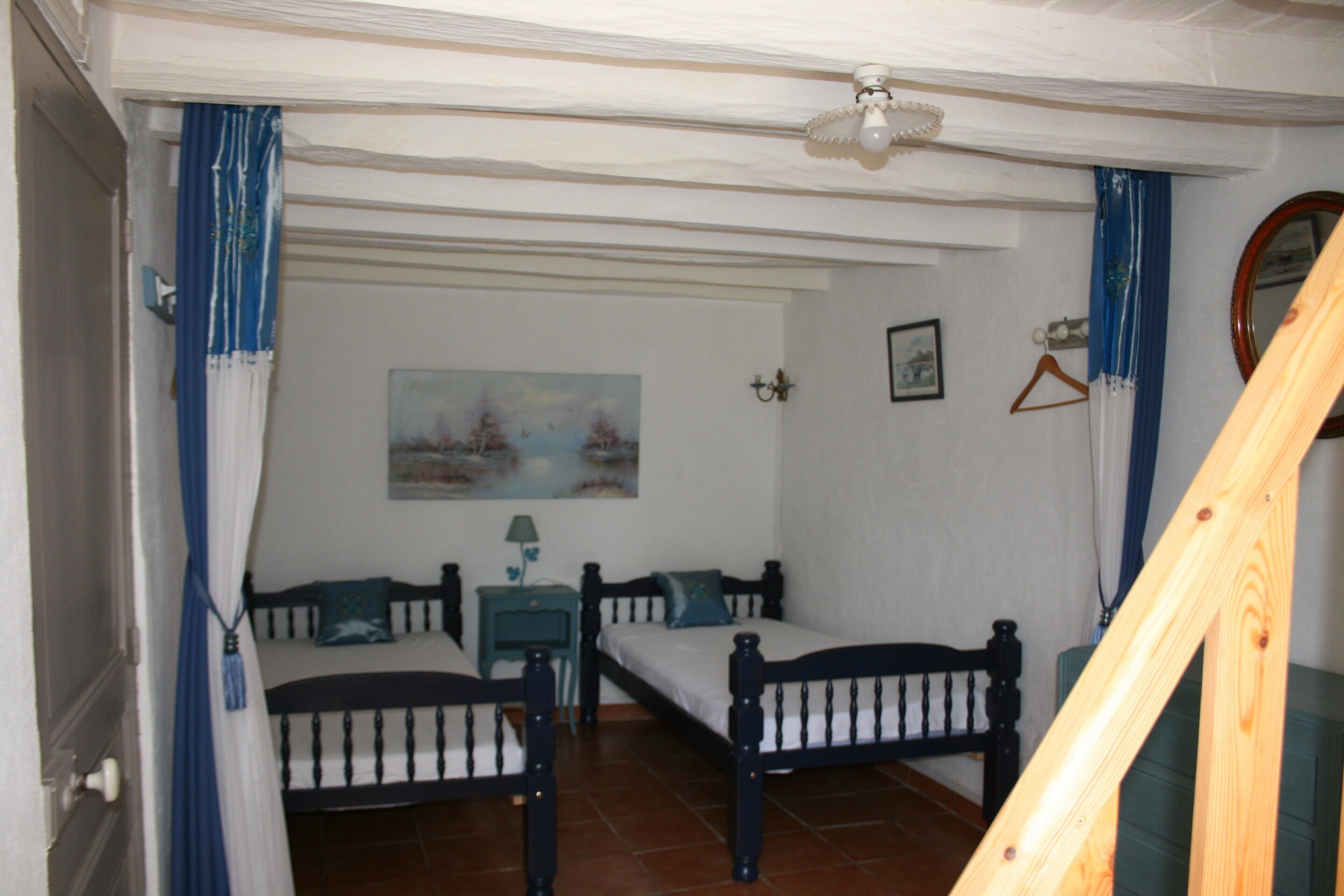 Un dormitorio con dos camas, un ventilador de techo, un cuadro y una escalera de madera.