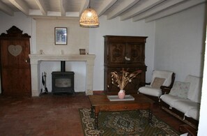A traditional living room with a fireplace, a wooden cabinet, a sofa, and a patterned rug. - Gîte le lit de la loire (Varennes-sur-Loire)