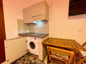 A compact kitchen with a washing machine, a sink, and a wooden table. - Practical Studio With Balcony by the Beach (Caorle)