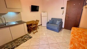 A compact living space with a kitchenette, a dining area, a sofa, and a patterned bedspread. - Practical Studio With Balcony by the Beach (Caorle)