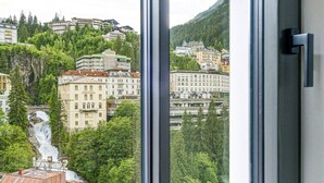 A window with a view of a cityscape, including buildings and a waterfall. - Waterfall View Penthouse · One-Bedroom (Residenz Boutique Suites (Bad Gastein))