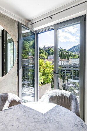 Ein moderner Balkon mit Glastür, einem Marmortisch und einem Topfpflanzen.
