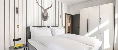 A modern hotel room with a large bed, a mounted deer head on the wall, and a wardrobe with sliding doors.