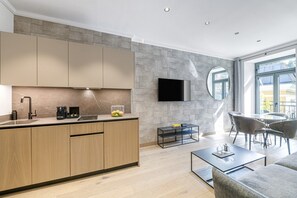 Eine moderne Küche mit Einbauofen, Kaffeemaschine und Obstschale. Es gibt einen Essbereich mit rundem Tisch und Stühlen sowie ein an der Wand befestigtes Fernsehgerät.