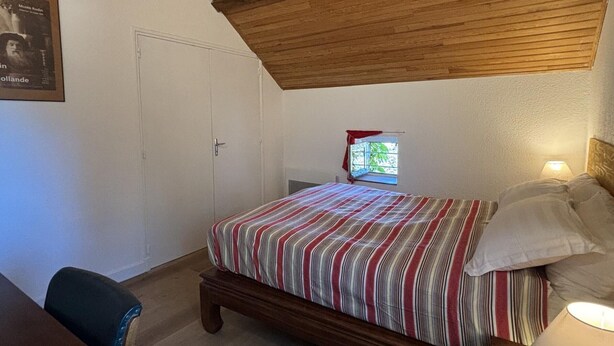 Een slaapkamer met houten plafond, een bed met gestreepte lakens, een raam met uitzicht en een deur.