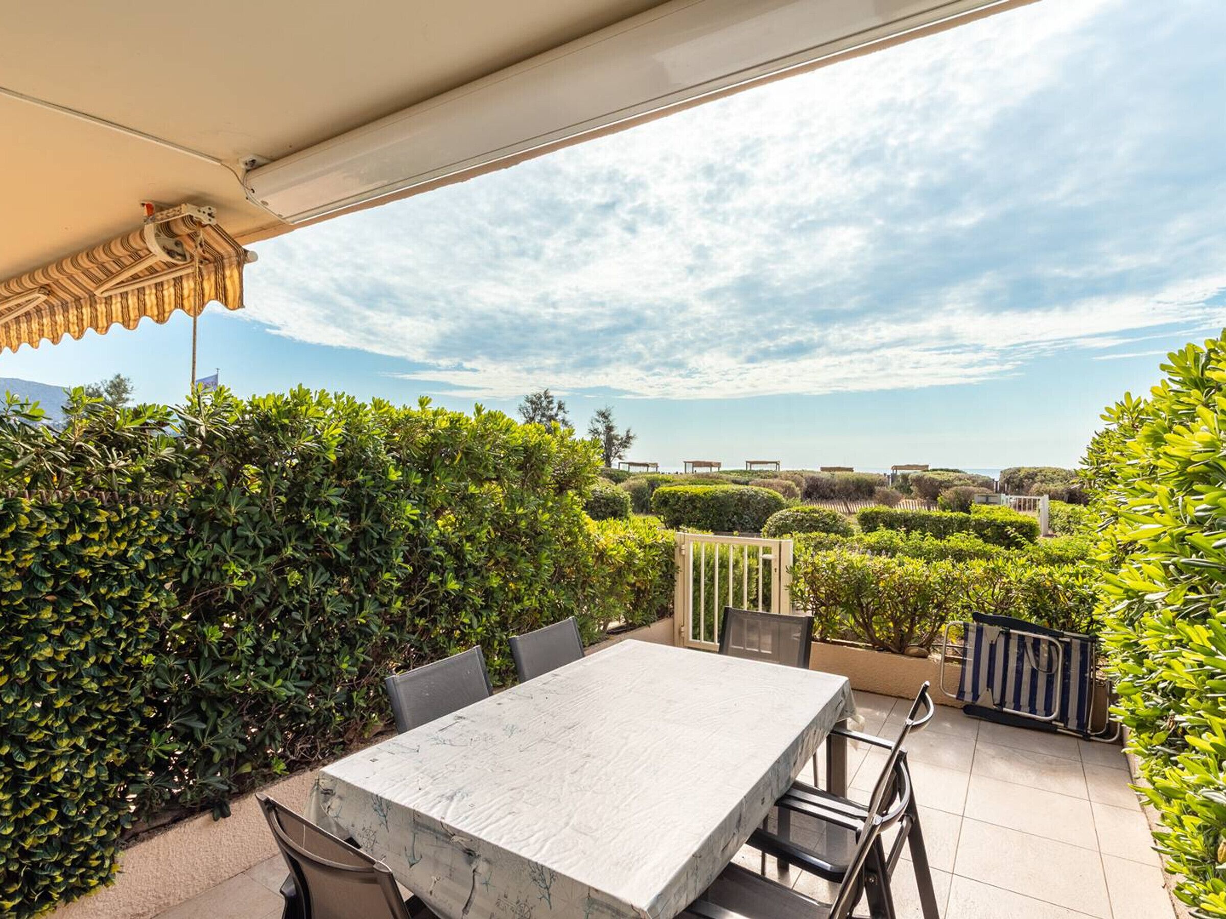 Eine Terrasse mit Tisch und Stühlen, umgeben von viel Grün und Blick aufs Meer.