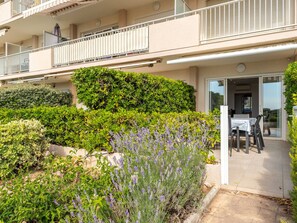 Um edifício residencial com varanda, pátio com mobiliário de exterior e diversas plantas, incluindo lavanda.