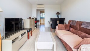 Ein modernes Wohnzimmer mit Flachbildfernseher, einer Couch, einem Couchtisch und einem Essbereich im Hintergrund.