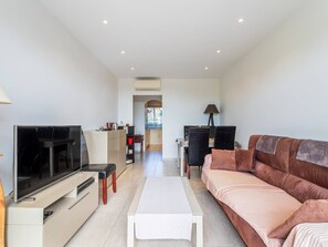 Ein modernes Wohnzimmer mit Flachbildfernseher, einer Couch, einem Couchtisch und einem Essbereich im Hintergrund.