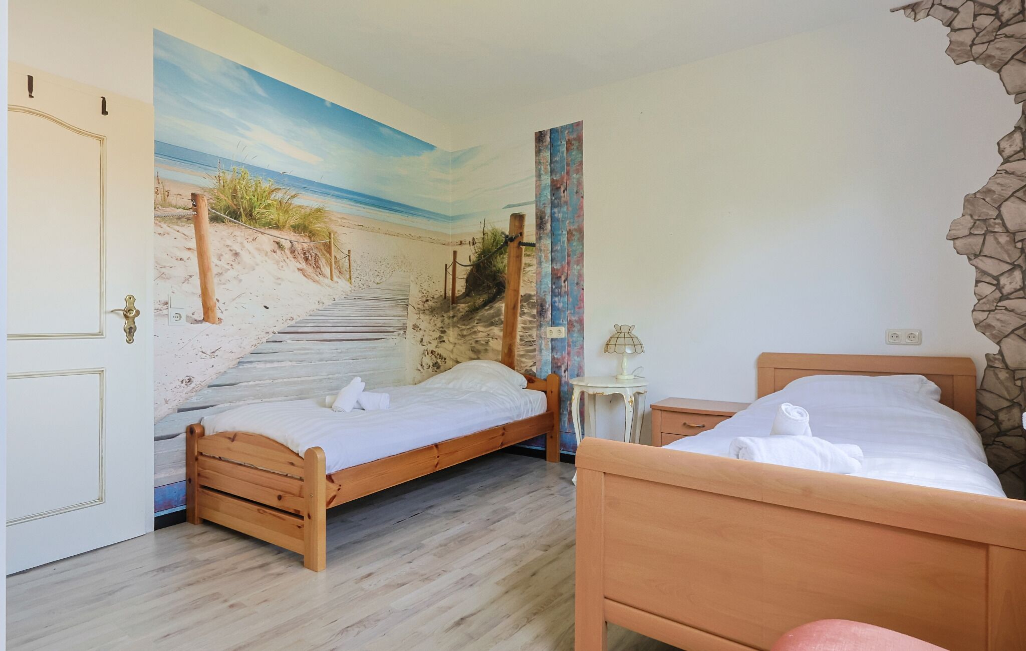 A room with two wooden beds, a beach mural on the wall, and a stone wall feature.