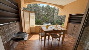 A balcony with a table and chairs, a grill, and a view of trees and a car. - Calm studio with private parking - 2 guests (Bandol)