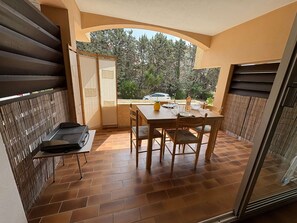 Ein Balkon mit Tisch und Stühlen, einem Grill und Blick auf Bäume sowie ein Auto.
