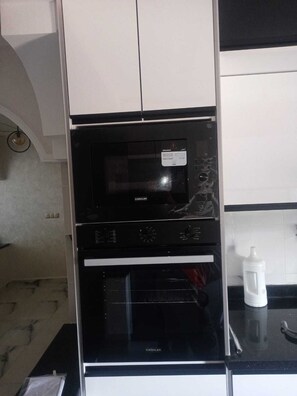 Una cocina con un microondas negro, un horno y un recipiente blanco sobre la encimera.