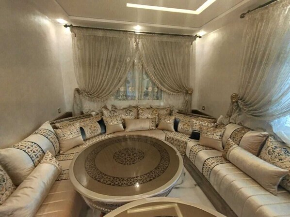 A round coffee table surrounded by a beige sofa set with patterned cushions.