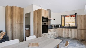 A modern kitchen with wooden cabinetry, a dining table, and a window with a view. - Renovated apartment mountain view - 2 guests (Saint-Pée-sur-Nivelle)