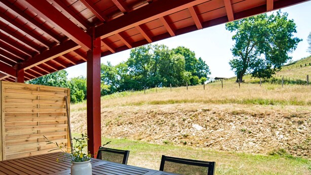 An outdoor wooden table with chairs, a potted plant, and a red roof structure. - Renovated apartment mountain view - 2 guests (Saint-Pée-sur-Nivelle)