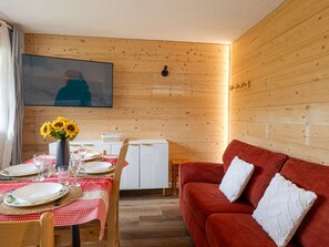 A cozy room with a dining table set for four, a red sofa, and a television mounted on the wall. - Ski-in/ski-out apartment - 6 guests (Plagne Villages)