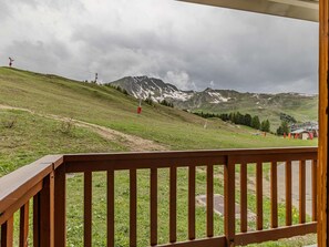 Vista desde un balcón de madera con vistas a una colina cubierta de hierba y una monta ña al fondo.