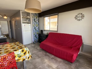 Ein kompakter Wohnbereich mit einer Küchenzeile, einem Essbereich mit Tisch und Stühlen, einem roten Sofa und einem Fenster, das für natürliches Licht sorgt.