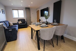 A dining area with a wooden table, four grey chairs, a sofa, and a TV mounted on the wall. - Relaxing Riverside Retreat (Gainsborough)