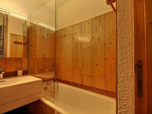 Ein Badezimmer mit Holzvertäfelung, einer weißen Badewanne, einer Duschkabine aus Glas und einem Spiegel über dem Waschbecken.