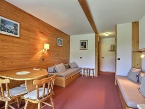 Ein gemütliches Zimmer mit Holzwänden, einem runden Holztisch mit Stühlen, einer Couch und einem kleinen Hocker.