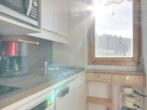 A kitchen with a coffee maker, a window with a view of trees, and a wooden shelf with kitchenware. - Cozy studio with direct slope access - 2/3 guests (Belle Plagne)