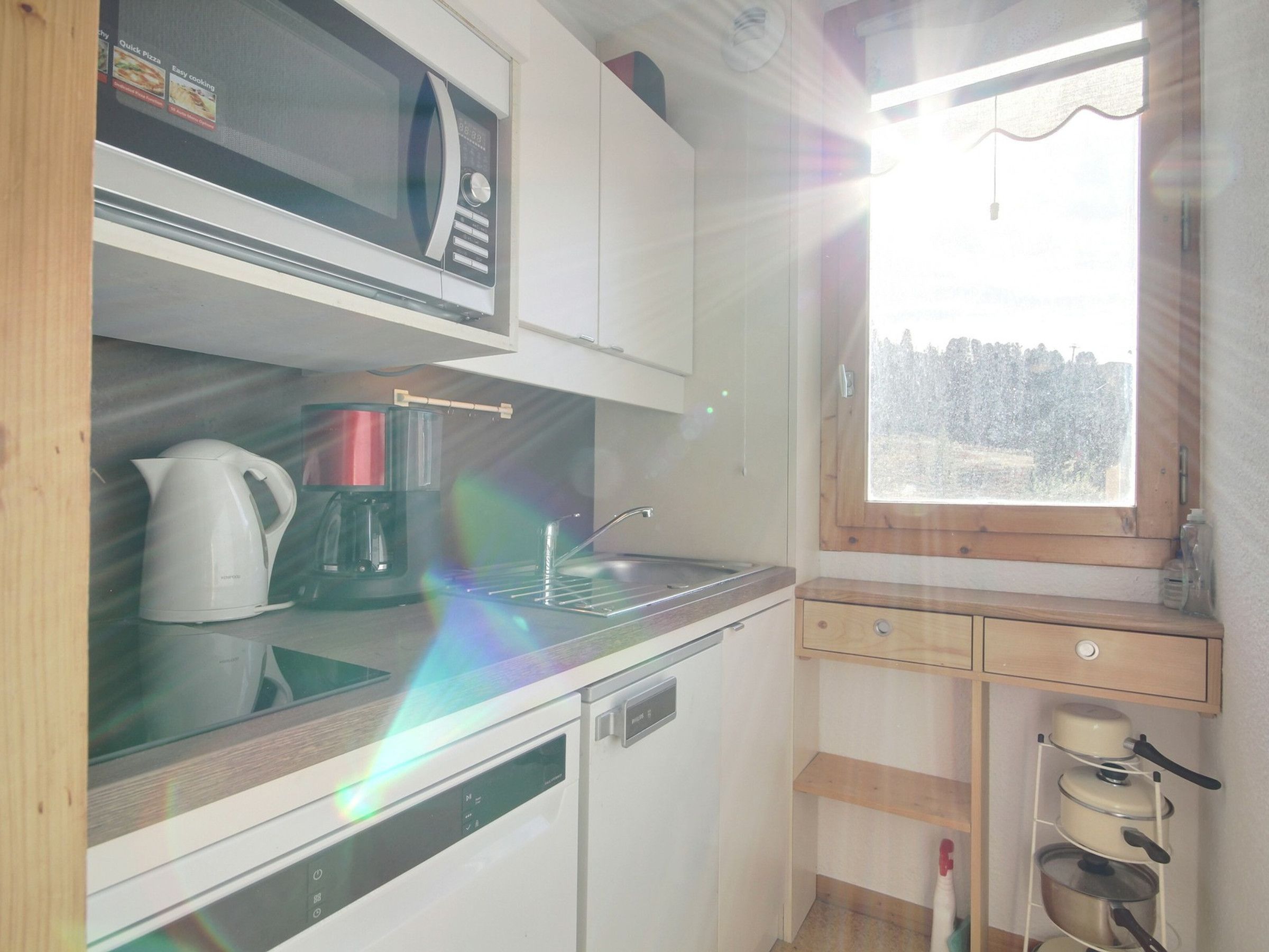 A compact kitchen with a microwave, coffee maker, and a window with a view of trees.