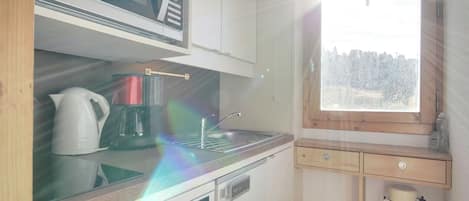 A compact kitchen with a microwave, coffee maker, and a window with a view of trees.