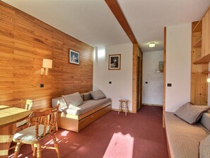 A cozy room with a wooden wall, a sofa, a small table, and a chair. - Cozy studio with direct slope access - 2/3 guests (Belle Plagne)