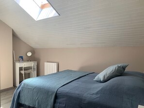 A bedroom with a sloped ceiling, a bed with a blue blanket, a desk with a mirror, and a radiator. - Quiet apartment near shops - 4 guests (Barcelonnette)