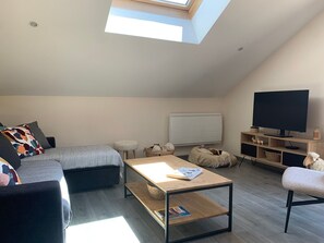 A loft-style bedroom with a skylight, a bed, a sofa, a coffee table, a TV, and a small dog bed. - Quiet apartment near shops - 4 guests (Barcelonnette)