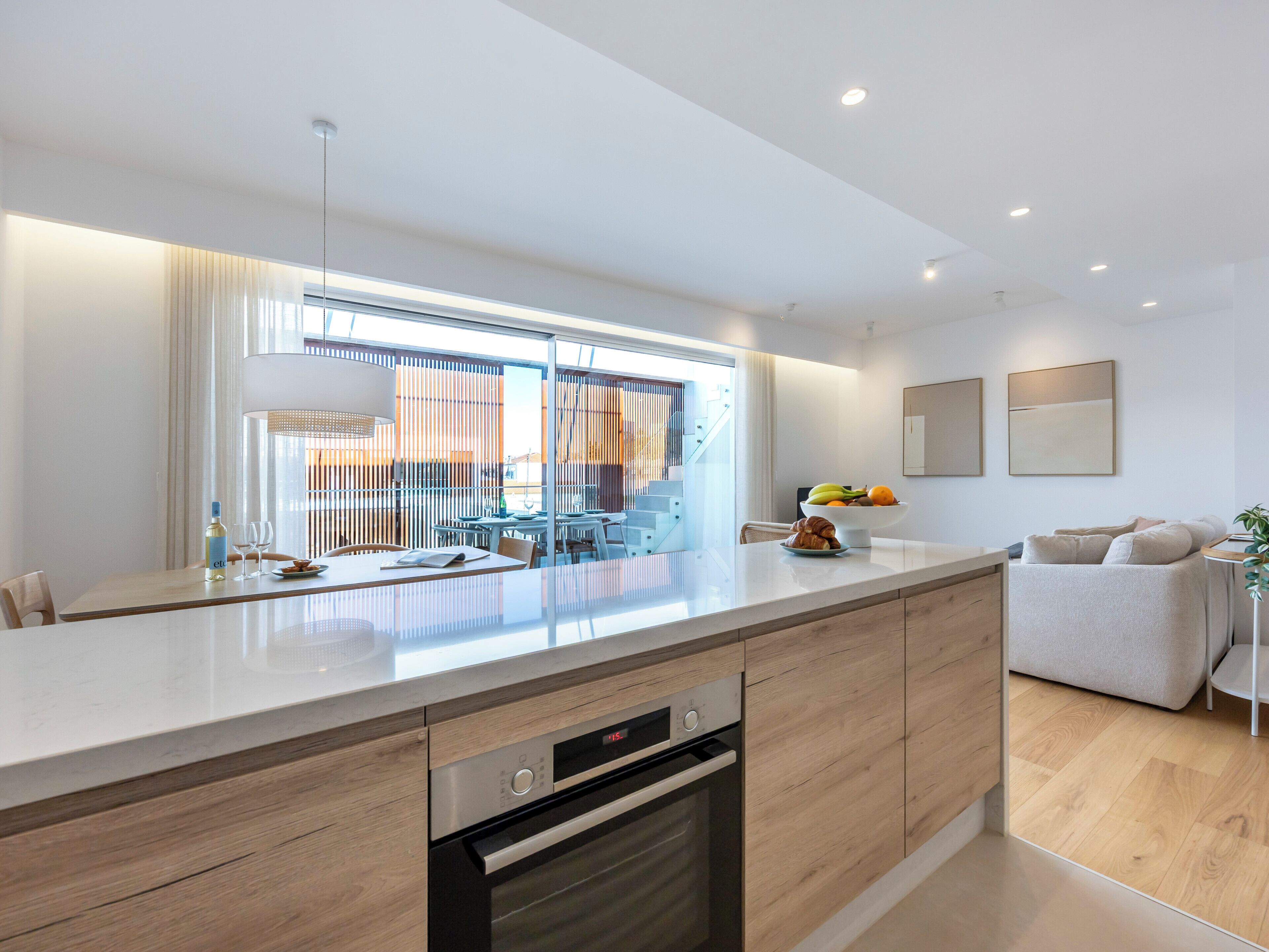 A modern kitchen with a built-in oven, a dining area with a table and chairs, and a staircase leading to an upper level.