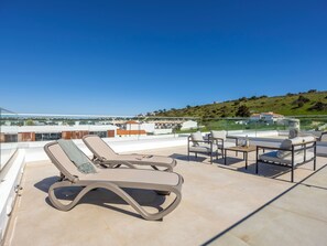 Eine Dachterrasse mit Liegestühlen und einem Tisch, mit Blick auf ein Wohngebiet und Hügel.