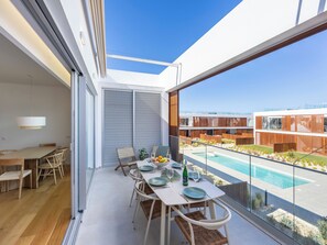 Ein moderner Essbereich mit Blick auf den Pool, ausgestattet mit einem Tisch für vier Personen, Korbstühlen und einem großen Fenster mit Poolblick.