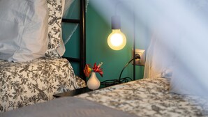 Un letto con biancheria a fiori, un vaso con fiori, una presa elettrica e una lampadina a sospensione.