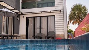 Un hotel moderno con piscina, lettini da relax e una terrazza coperta.