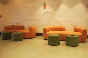 A modern interior with orange sofas and green ottomans, geometric wall designs, and a small statue. - The Landmark Maan Palace Hotel (Jaipur)