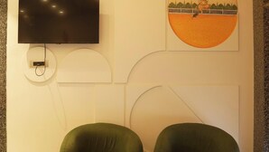 Een modern interieur met een flatscreen televisie aan de muur, een rond schilderij en beklede zitplaatsen in groene tinten.