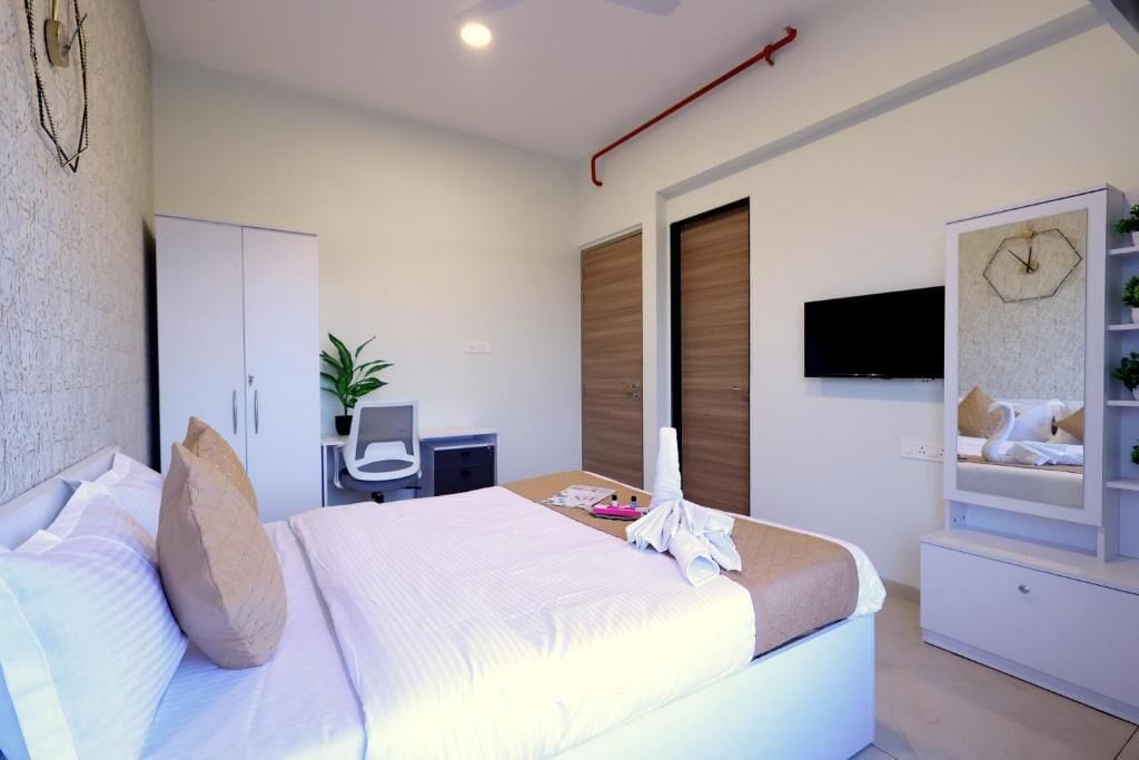 A modern bedroom with a bed, a desk, a chair, a TV, and a wardrobe.