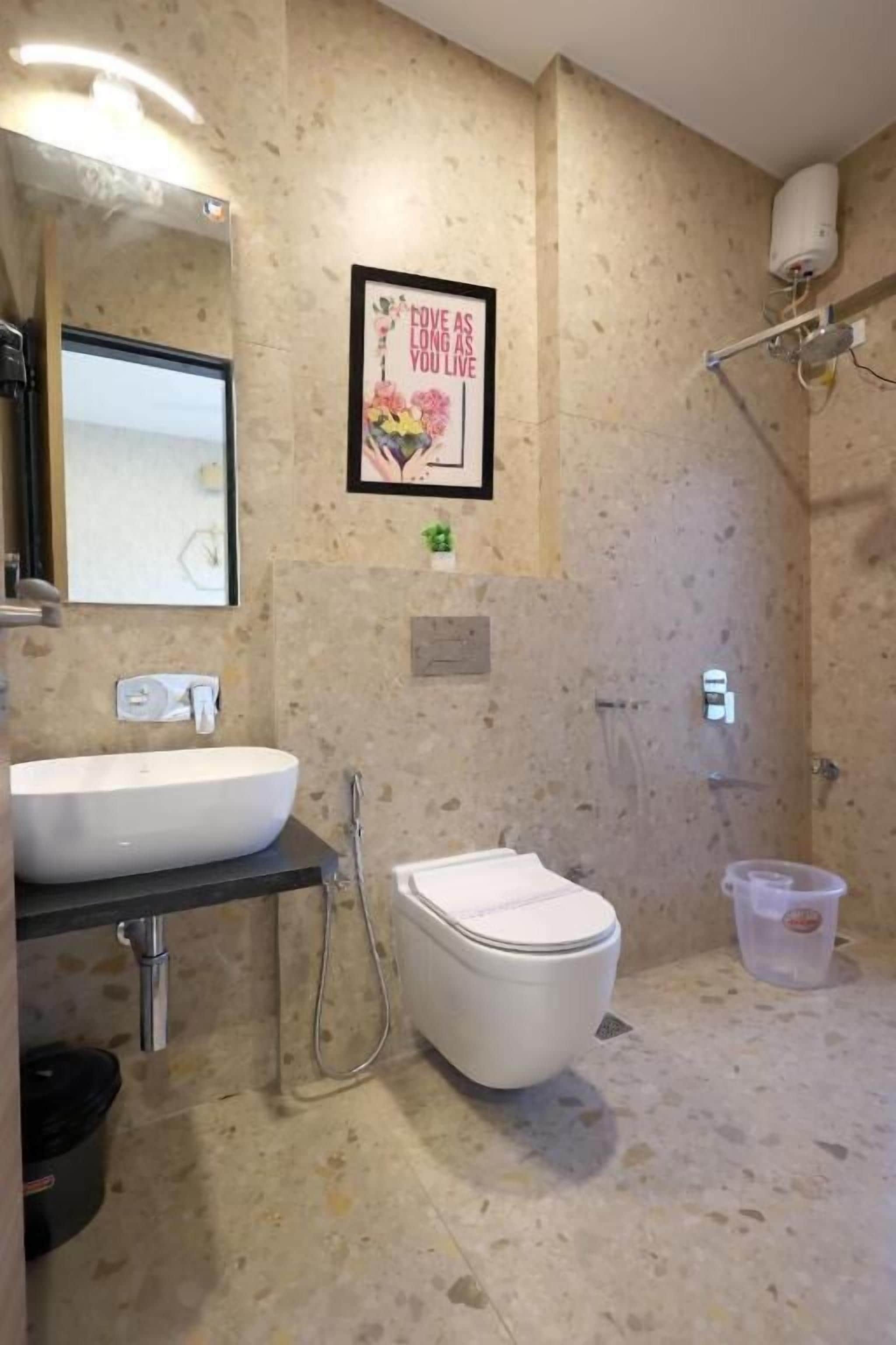 Ein Badezimmer mit Waschbecken, Toilette und Dusche. An der Wand hängt ein gerahmtes Bild und ein kleiner Mülleimer steht bereit.