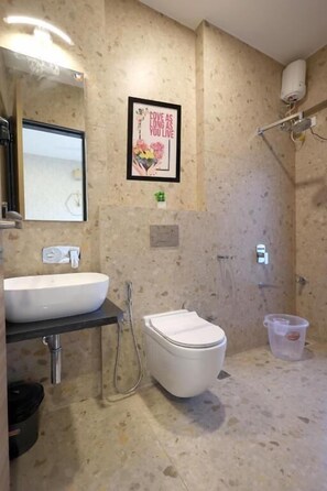 Baño con lavamanos, inodoro y ducha. Se observa un cuadro en la pared y un pequeño cubo de basura.