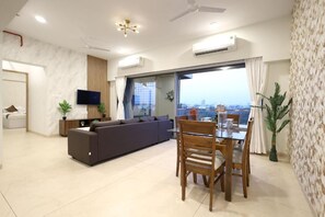 Uma sala de estar moderna com sofá, mesa de jantar, cadeiras, TV e varanda com vista para a cidade.