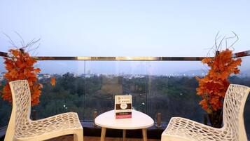 Een balkon met twee rieten stoelen, een kleine tafel, een bordje en uitzicht op een stadsgezicht.