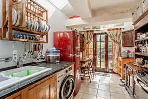 A kitchen with a washing machine, a refrigerator, and a dining area with a table and chairs. - Host & Stay | The 1890 Petersfield Retreat (Cambridge)