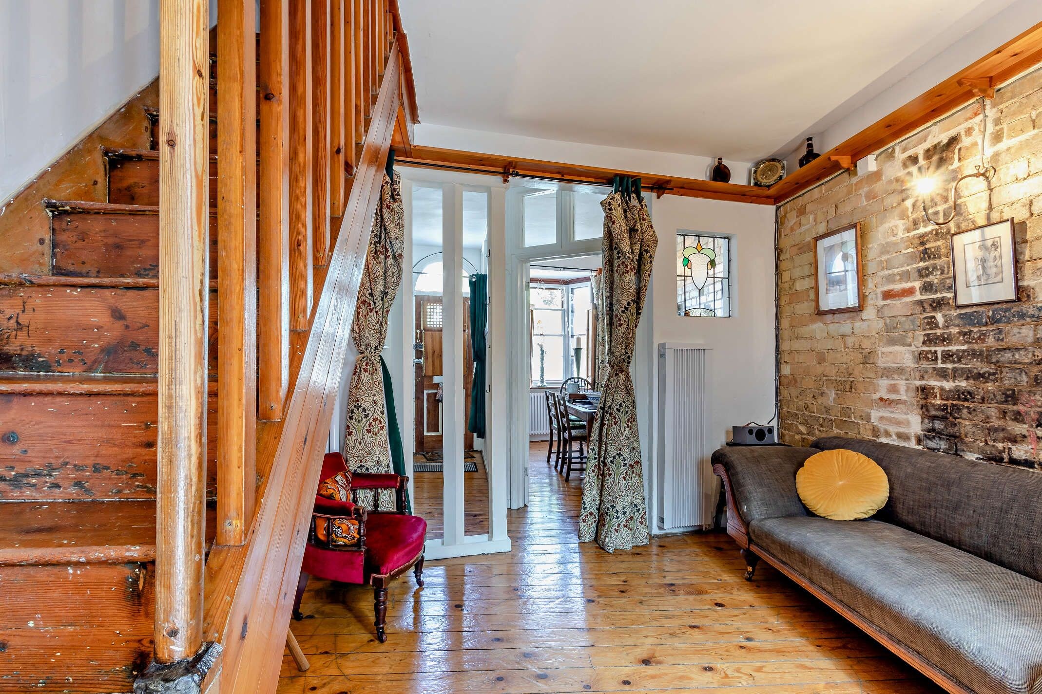 Una escalera de madera que conduce a una habitación con pared de ladrillo, un sofá y una cortina estampada.