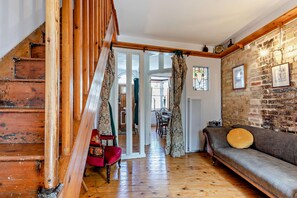Una escala de fusta que mena a una habitació amb una paret de maó, un sofà i una cortina amb dibuixos.