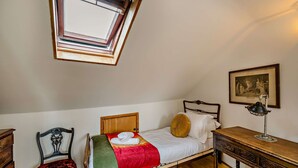 Een kamer met een enkel bed, een houten bureau, een stoel, een lijst met een foto aan de muur en een dakraam.