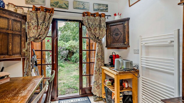 Een keuken met een houten tafel, een koffieapparaat en een broodrooster. Er is een deur naar een tuin.