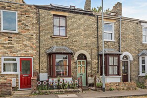 A two-story brick house with a red door, a green door, and a window with a white frame. - Host & Stay | The 1890 Petersfield Retreat (Cambridge)